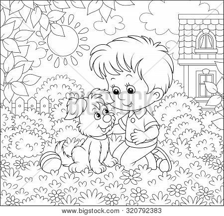 Little Boy Playing With A Small Pup Among Flowers On A Lawn In Front Of His House On A Sunny Summer 