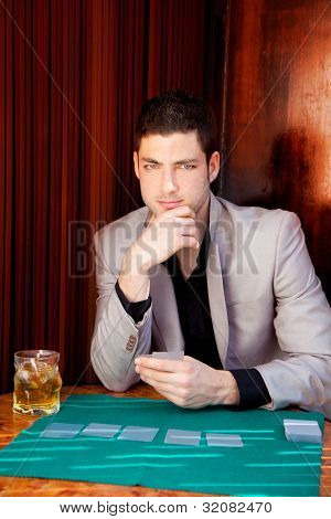 Uomo latino bello giocatore nel tavolo poker carte da gioco e bere whisky
