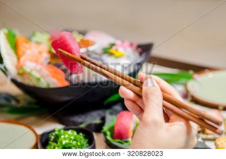 Hand Holding Wooden Chopsticks Tongs Tuna Sashimi At Japanese Food Restaurant.