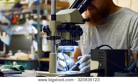 Repairman Looks Through Microscope Produces Solders On Circuit Board Of Device.