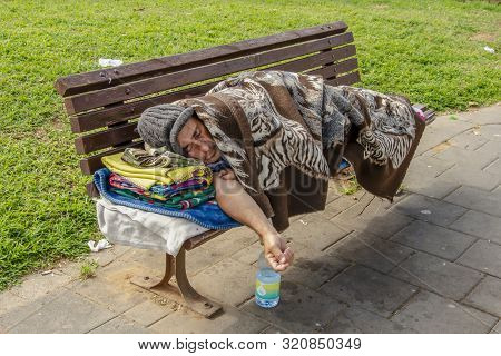 Tel-aviv, Israel, 07.04.2018: Homeless Beggar Man With A Bag Lying On Bench Outdoors In City, Sleepi