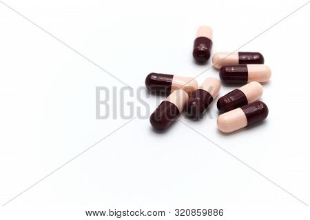 Prescription Drugs, Capsules Of Soft Pink And Dark Reddish Brown Colors All Mixed In. On White Backg