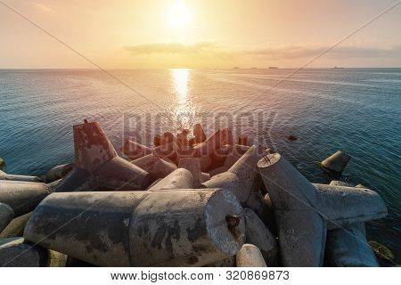 Beautiful Sunset Seascape. Breakwaters Tetrapods Ashore Of Pier. Cargo Ships On The Horizon. Travel 