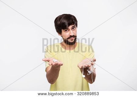 Pretty Brunet Bearded Man With Whiskers Holds Wired Headphones In One Hand And Wireless Earbuds In A