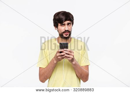 Handsome Brunet Bearded Man With Whiskers In A Yellow Tee Holding Smartphone Expressing Emotion Of D