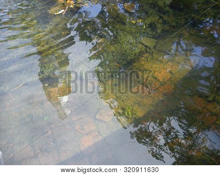 Reflection Of Blue Sky And Trees In The Clear Water Of A Fountain In A City Park. The Stone Bottom O