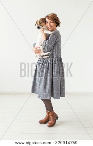 Charming Smiling Young Woman In A Stylish Gray Dress Holding Her Favorite Dog Jack Russell Terrier. 