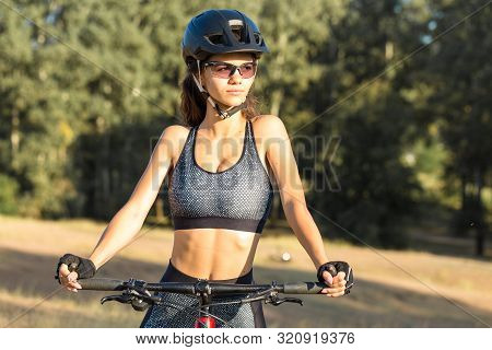 Girl On A Mountain Bike On Offroad, Beautiful Portrait Of A Cyclist At Sunset, Fitness Girl Rides A 