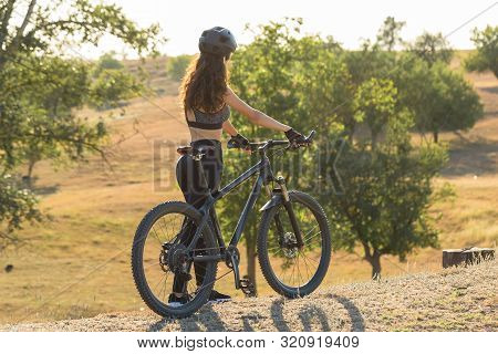 Girl On A Mountain Bike On Offroad, Beautiful Portrait Of A Cyclist At Sunset, Fitness Girl Rides A 