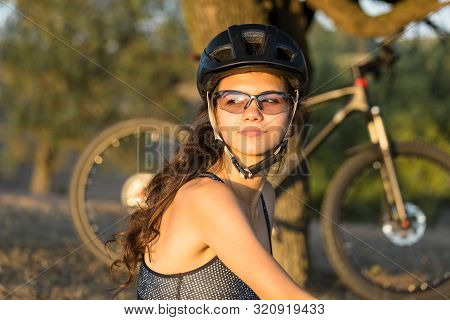 Girl On A Mountain Bike On Offroad, Beautiful Portrait Of A Cyclist At Sunset, Fitness Girl Rides A 