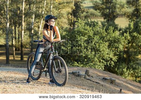 Girl On A Mountain Bike On Offroad, Beautiful Portrait Of A Cyclist At Sunset, Fitness Girl Rides A 