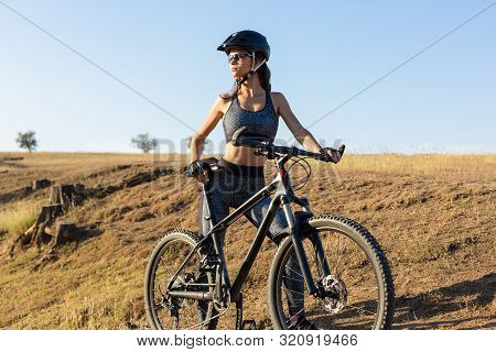Girl On A Mountain Bike On Offroad, Beautiful Portrait Of A Cyclist At Sunset, Fitness Girl Rides A 