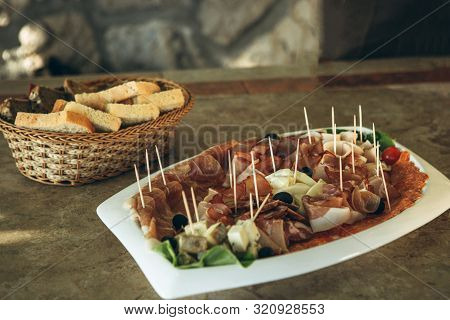 Plate With Various Meat Snacks And Cheese. In The Background Is A Plate Of Bread.
