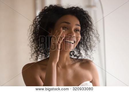 Smiling Biracial Woman Apply Under Eye Cream Looking In Mirror
