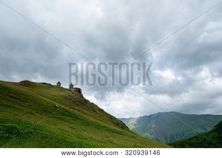 Gergeti Trinity Church Or Tsminda Sameba, Dramatic Landscaoe With Clouds. Gergeti Church Stands Near