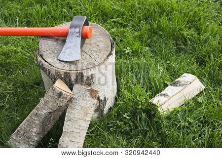 Stump With An Splitting Axe And Firewood On The Grass. Birch Logs
