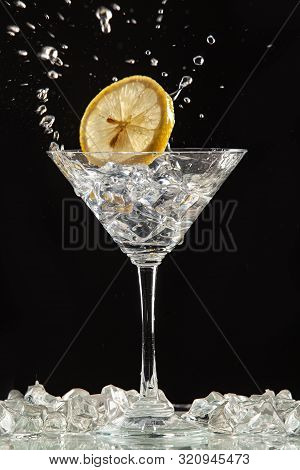 Glass Of Water, Lemon And Watersplashes On A Black Studio Background