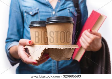 Two Paper To Go Coffee Cups In Women's Hand. Student With Takeaway Coffee Cups And Book In Her Hands