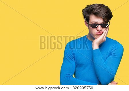 Young man wearing funny life glasses over isolated background thinking looking tired and bored with depression problems with crossed arms.