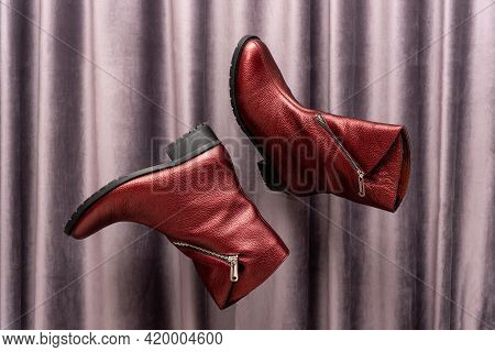 Levitating Shoes. Red Leather Womens Boots Flying In Air Against Grey Draped Textile Fabric Or Curta