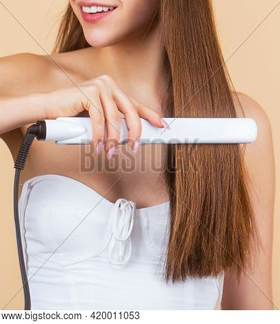 Smiling Woman Ironing Long Hair With Flat Iron. Portrait Of Young Beautiful Girl Using Styler On Her