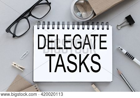 Delegate Tasks. Gray Background. Text On Notepad Near Glasses With Pen And Pencil. Business Layout.