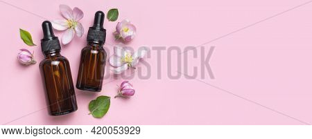 Clean Brown Glass Cosmetic Bottles With Dropper, Delicate Spring Flowers On Pink Background Flat Lay