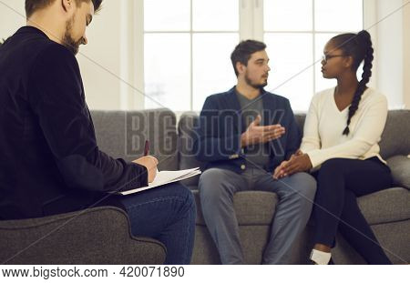 Family Consultant Writing Notes While Couple Discussing Relationship Problem