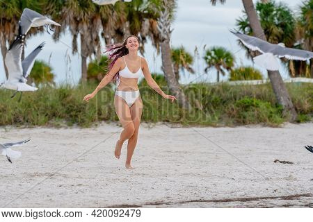 A beautiful brunette bikini model enjoys the weather outdoors on the beach while chasing seagulls