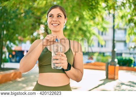 Young blonde sportswoman doing exercise drinking bottle of water at the city.