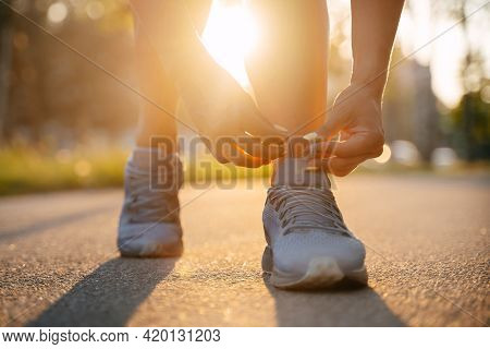 Running Woman Tying The Laces Of Sneakers Before Jogging On The Road In The Park In Sunny Weather, T