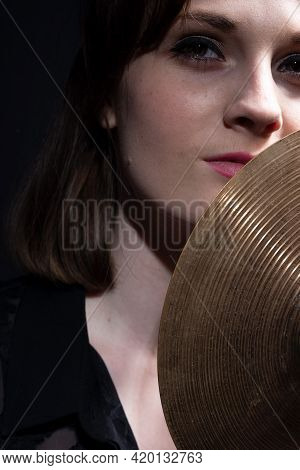 Girl Drummer Holding A Small Drum Cymbal In Her Hands. Dramatic Portrait On Black Background Beautif