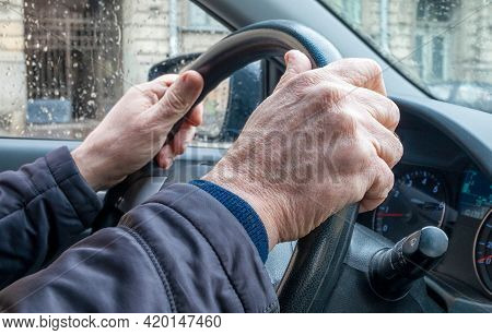 Close-up Of The Hand Of An Adult Man In A Passenger Car, Holding The Steering Wheel In Cold Rainy We