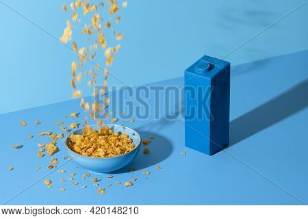 Pouring Cereals In A Bowl On A Blue Colored Table. Breakfast Table With Cornflakes Cereals In A Bowl