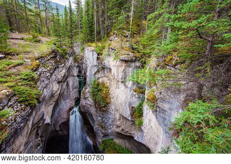 Powerful waterfall in a picturesque gorge Maligne Canyon. The sheer canyon walls and the seething icy water below. Cool cloudy day. Travel to the Rocky Mountains.