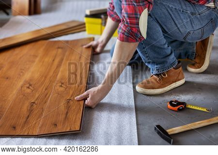Man worker installing laminate flooring. Wooden laminate floor plank and tools with male hand