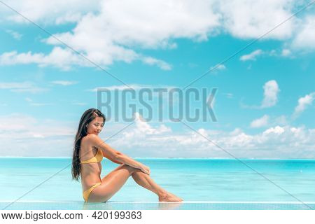 Spa body wellness therapy Asian beauty swimsuit model woman on luxury pampering thalasso pool resort relaxing sunbathing, sun tan skincare. Blue ocean sky background.
