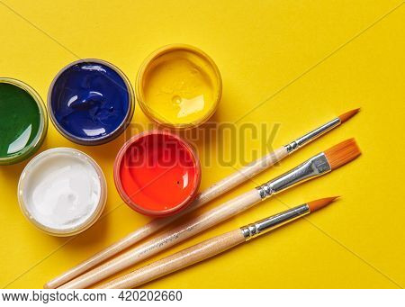 Three Brushes And Bright Cans Of Paint On A Yellow Background