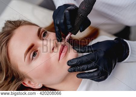 Permanent makeup master conturing lips in beauty salon. Side closeup view of tattoo process