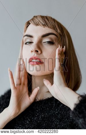 Brown hair woman in a black fluffy sweater touching her cheeks