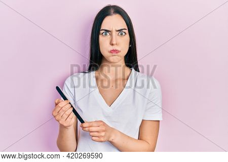 Beautiful woman with blue eyes using file nail puffing cheeks with funny face. mouth inflated with air, catching air. 
