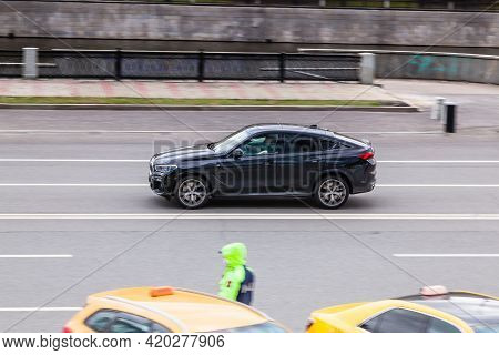 Side View Rolling Shot With Black Car In Motion. Bmw X6 Crossover Driving Along The Street With Blur