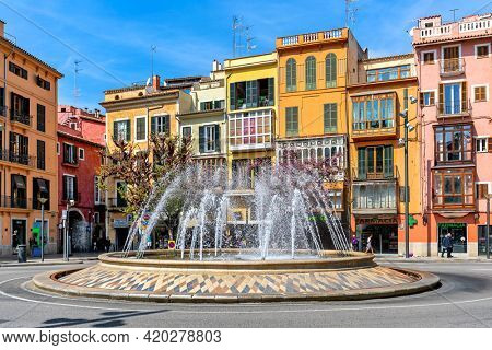 PALMA, SPAIN - APRIL 12, 2019: Fountain and colorful building on Plaza de la Reina - one of the famous and popular places located in the historical and tourist centre of Palma de Mallorca.