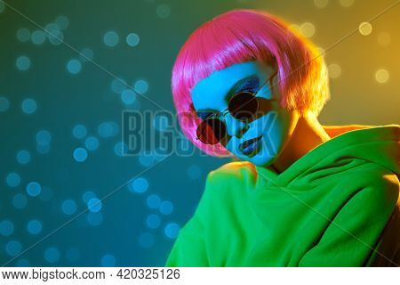 Modern girl with bright makeup and pink hair poses in red sunglasses and yellow suit in mixed color light. Sport chic fashion. Youth fashion and beauty trends. 