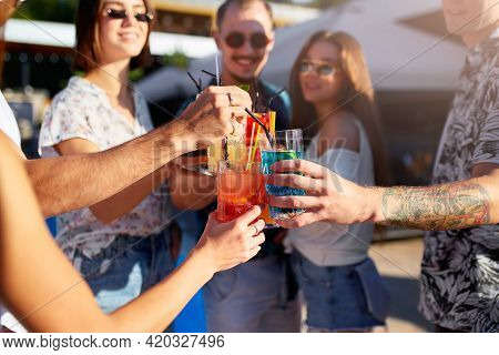Group Of Friends Having Fun At Poolside Summer Party, Clinking Glasses With Colorful Summer Cocktail