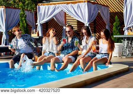 Group Of Friends Having Fun At Poolside Party Clinking Glasses With Fresh Cocktails Splashing Water 