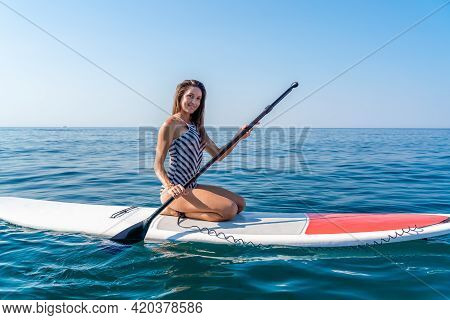 Sporty Girl On A Glanders Surfboard In The Sea On A Sunny Summer Day. In A Striped Swimsuit, It Is I