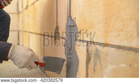 A Worker Plasters The Wall With A Spatula And Applies A Cement Mix Solution. The Repairman Lays The 