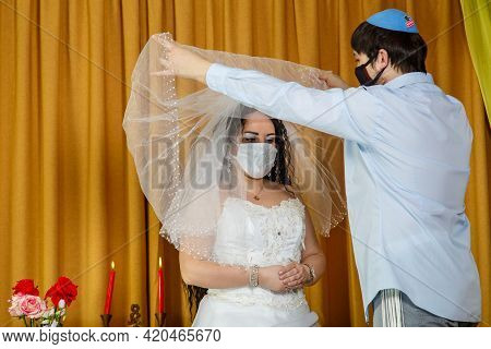 During The Chuppah Ceremony In The Synagogue, The Masked Bride And Groom Lifts The Veil From The Bri