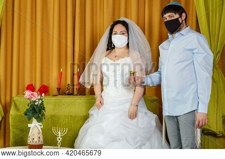 During The Chuppah Ceremony In The Synagogue, The Bride And Groom Stand Next To The Groom Holding A 